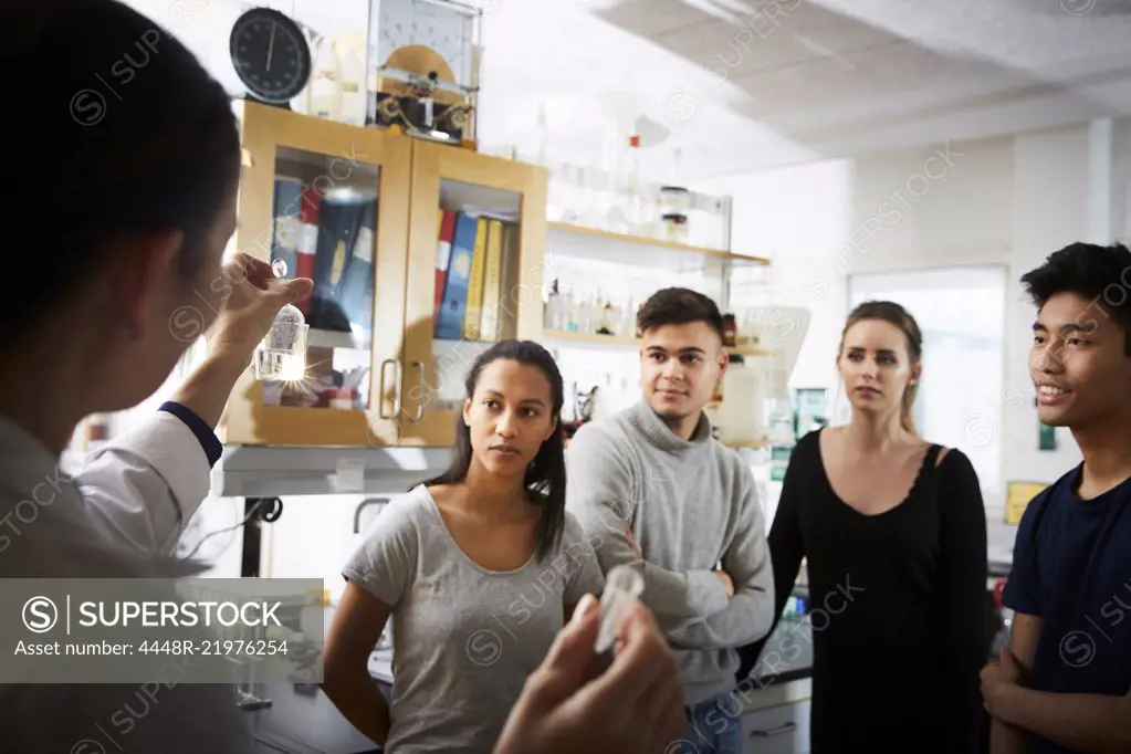 Rear view of mature female teacher showing solution while explaining to young multi-ethnic students in laboratory