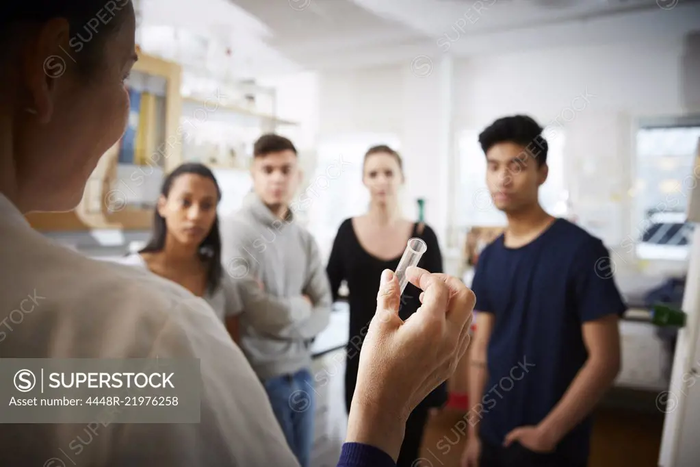 Rear view of mature female teacher holding test tube explaining to young multi-ethnic students in laboratory