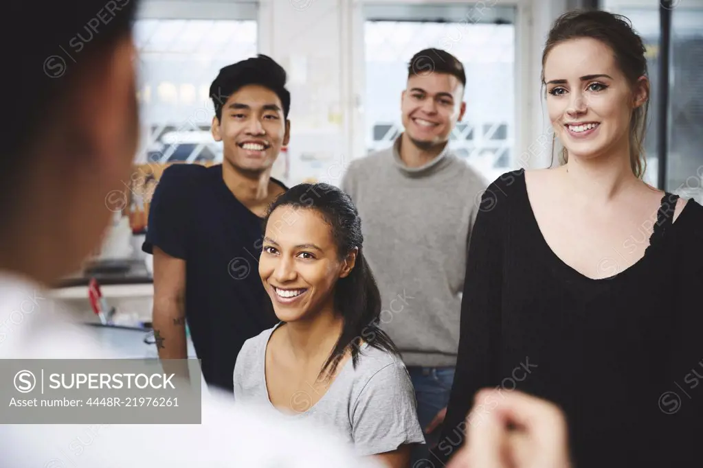 Happy multi-ethnic students looking at female teacher in chemistry laboratory