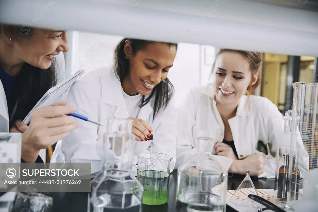 Smiling multi-ethnic university students with mature teacher mixing solution in laboratory