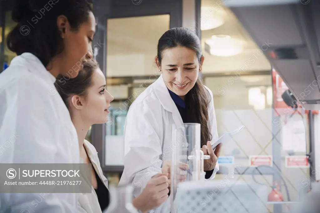 Smiling mature teacher with young female students learning chemistry at laboratory