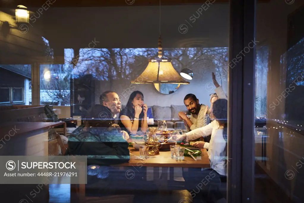 Multi-generation family talking while having dinner at table seen through window