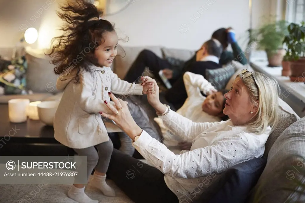 Girl playing with grandmother on sofa by family at home