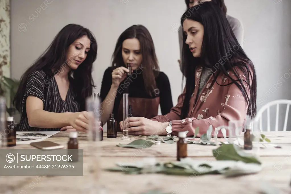 Female colleagues preparing perfume pipette at table in workshop