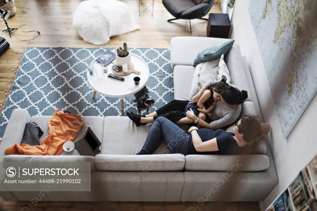 High angle view of lesbian couple talking with daughter while sitting on sofa by dog in living room at home