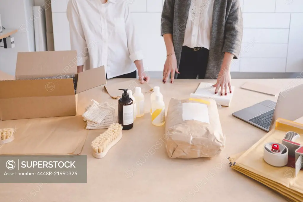 Midsection of female entrepreneurs standing with various manufacturing objects on table in workshop