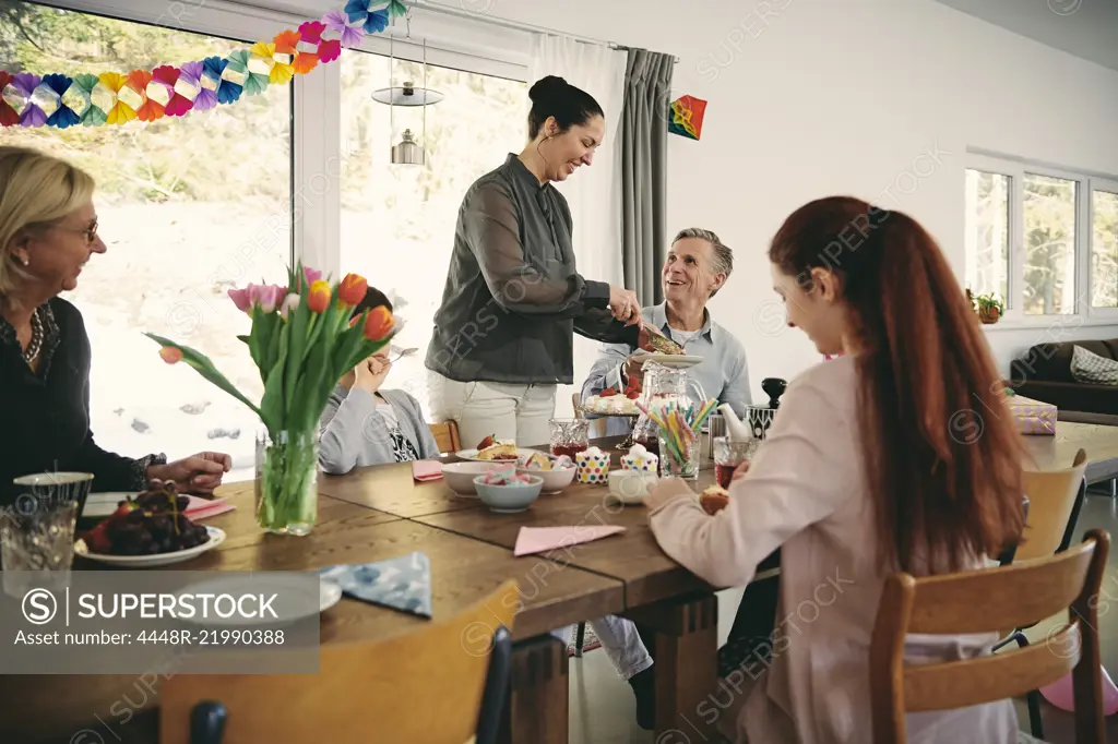 Smiling woman serving food to family during birthday party