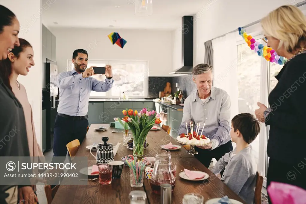 Man photographing boy with family during birthday party through smart phone