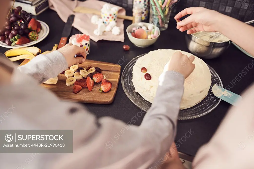 Cropped image of siblings decorating cake at kitchen counter