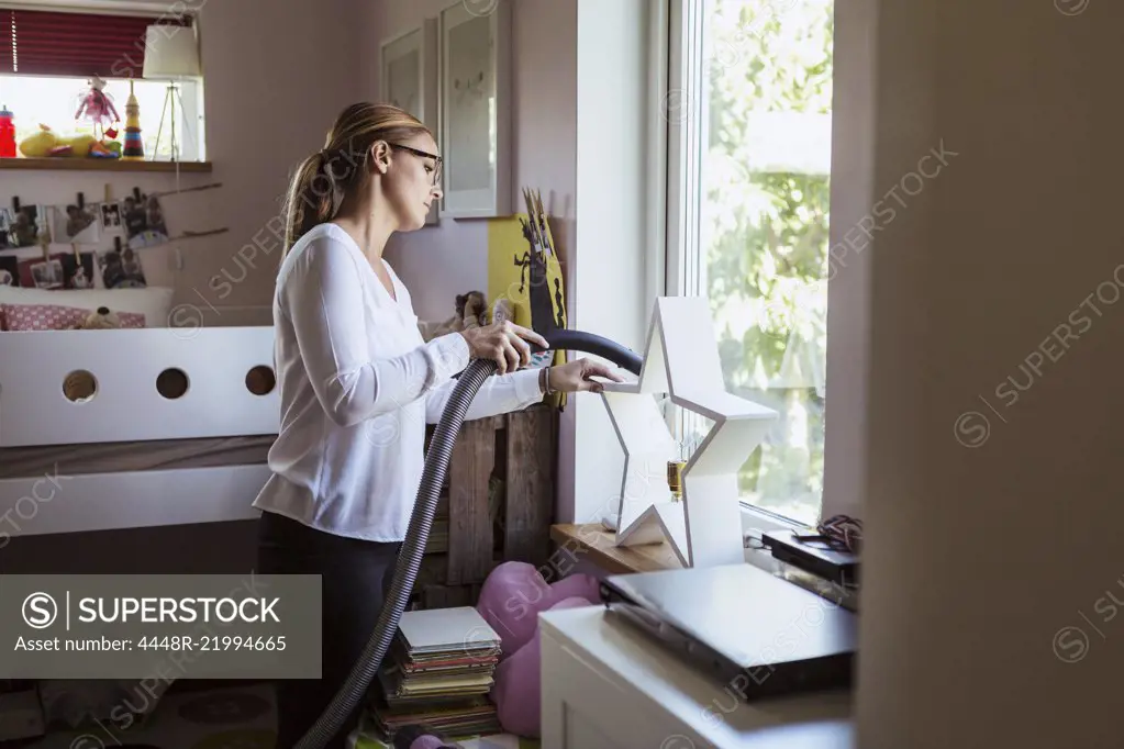 Woman cleaning bedroom with vacuum cleaner at home