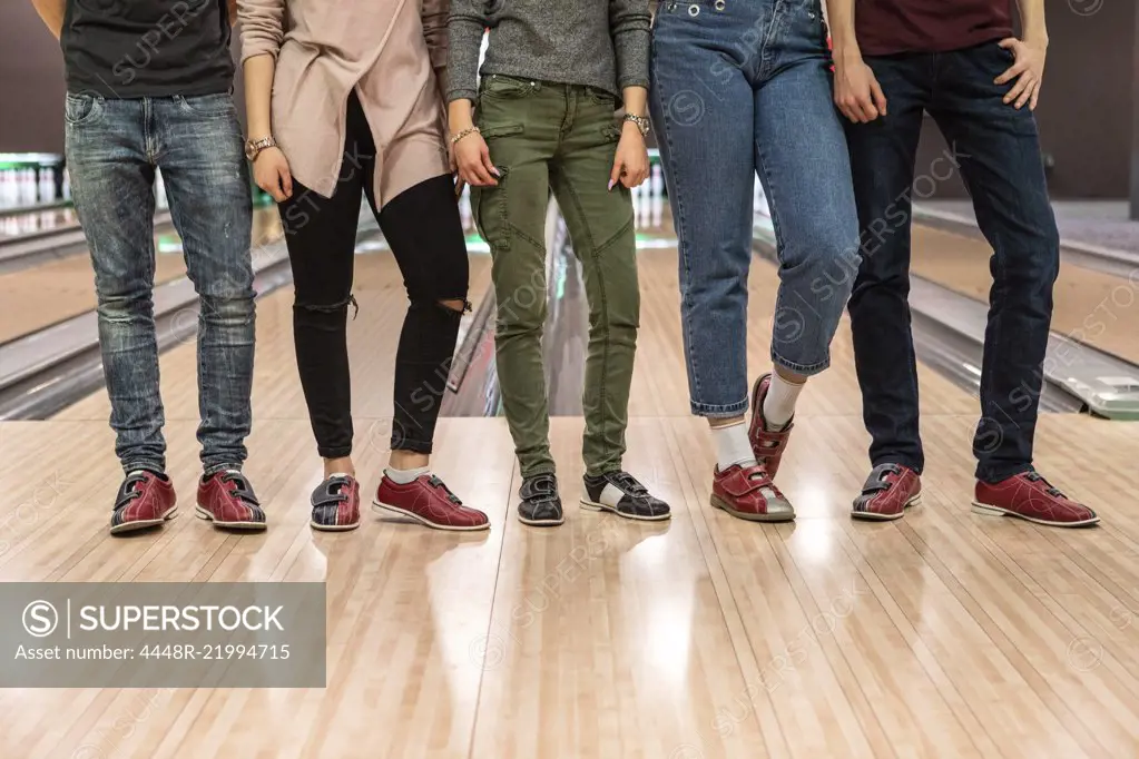 Low section of multi-ethnic friends standing on parquet floor at bowling alley