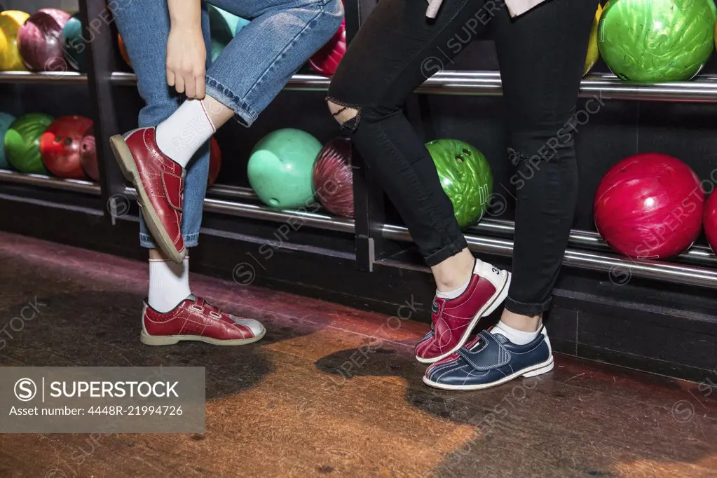 Low section of female friends wearing shoes standing by bowling rack