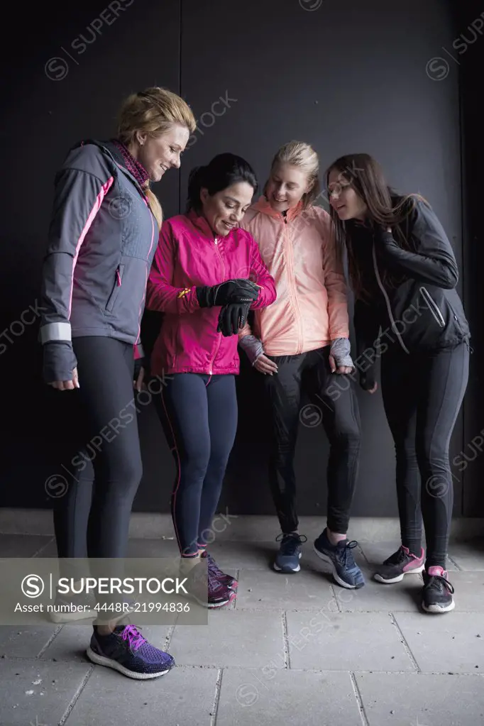 Full length of woman showing smart watch to friends while standing against wall in winter