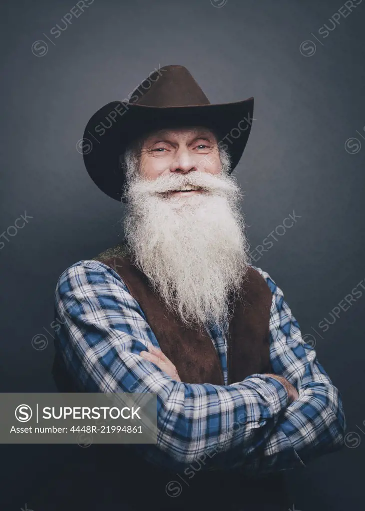 Portrait of happy senior man wearing cowboy hat against gray background