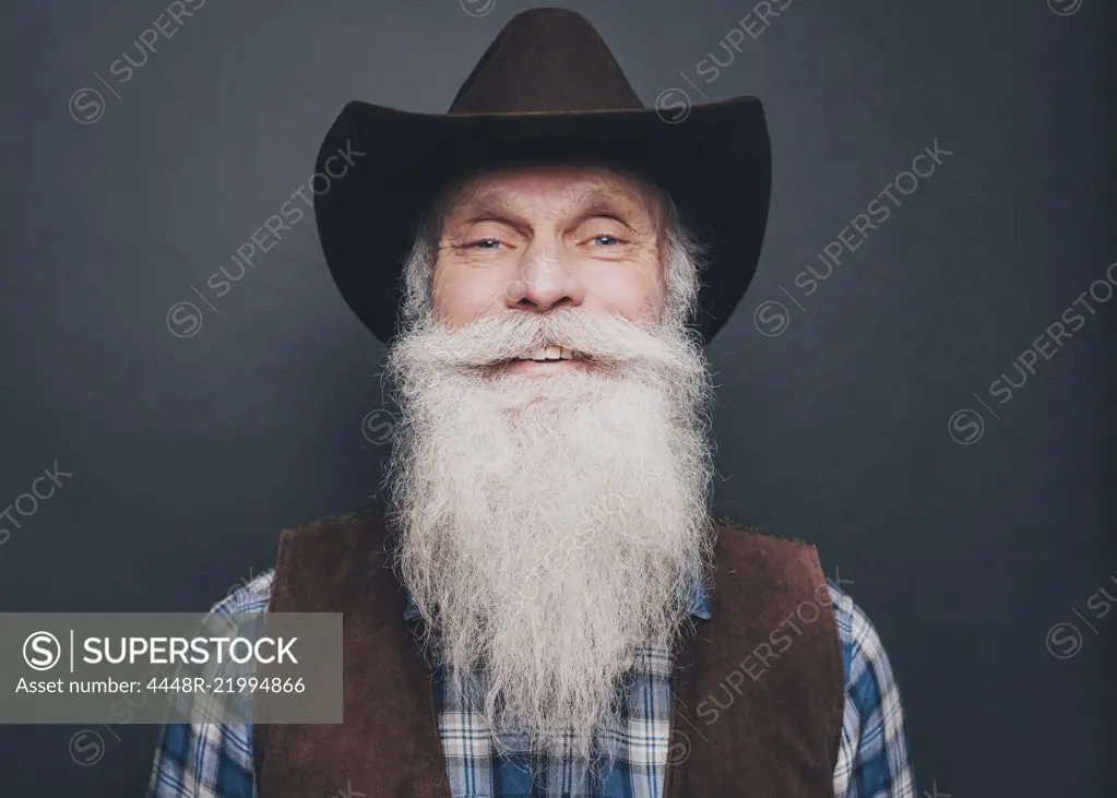 Portrait of happy bearded senior man wearing cowboy hat on gray background