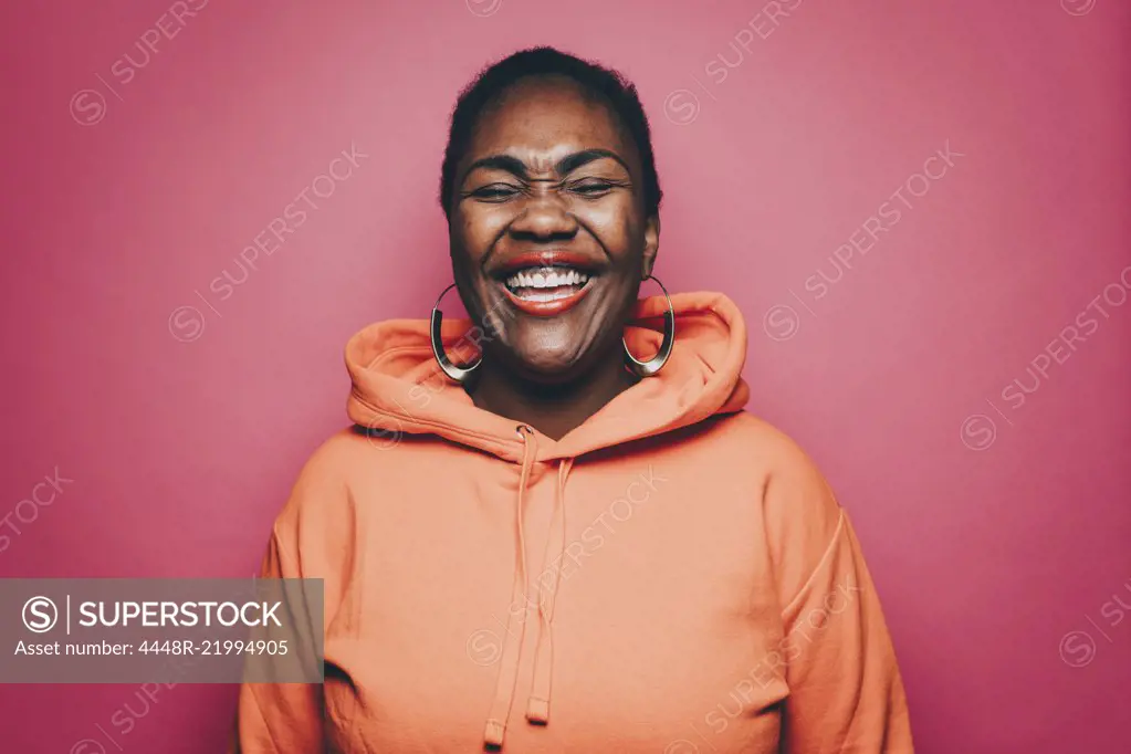 Cheerful mid adult woman wearing orange hooded shirt over pink background