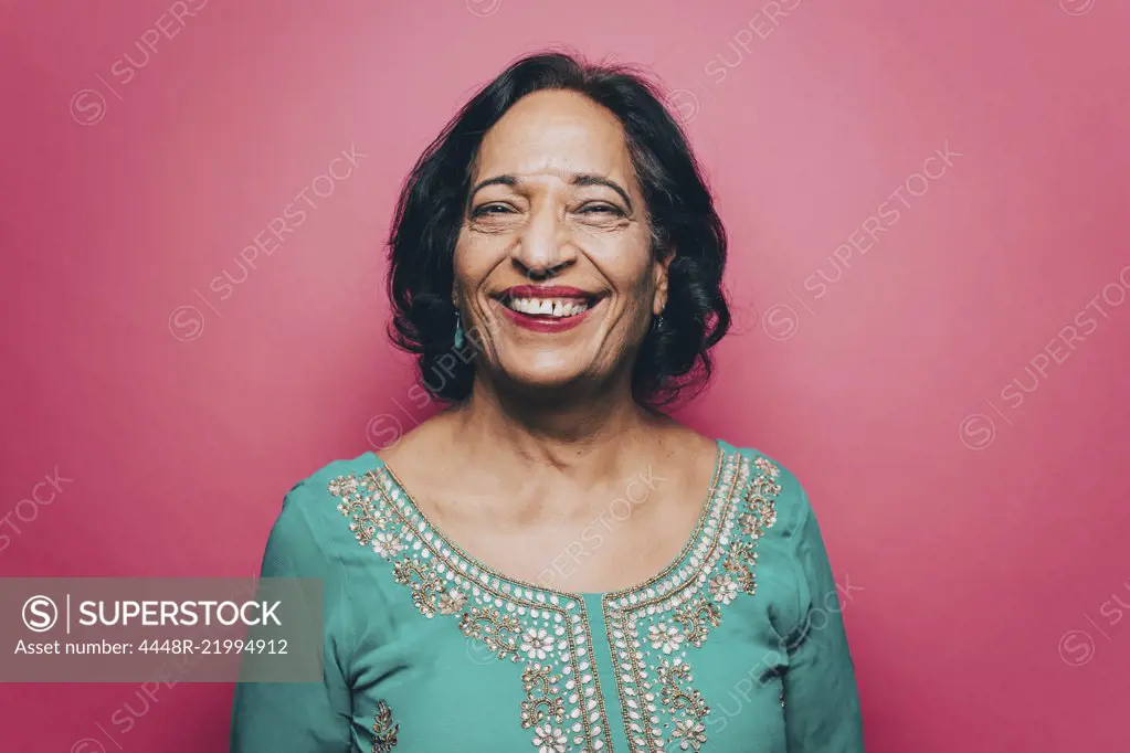 Portrait of smiling senior woman wearing salwar kameez against pink background