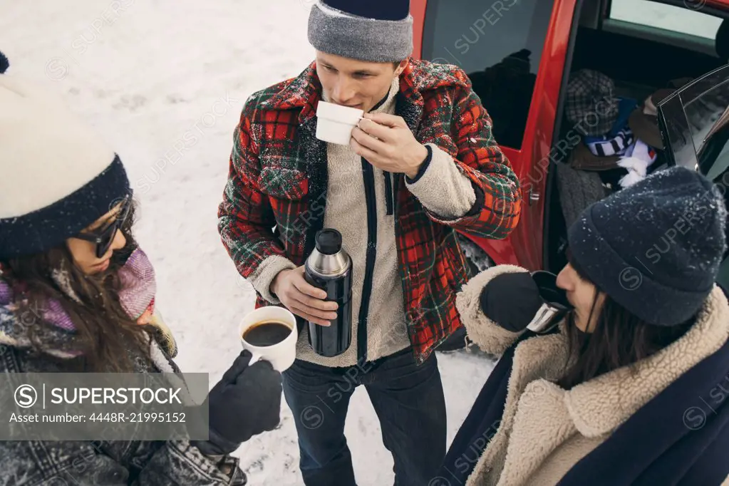 High angle view of friends having coffee while talking by car on snow