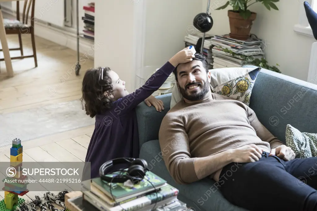 High angle view of girl keeping toy block on father's head lying on sofa at home