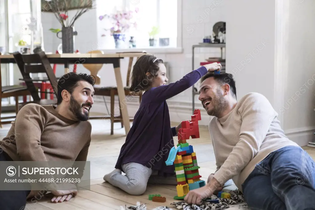 Cheerful fathers and daughter playing with toy blocks at home