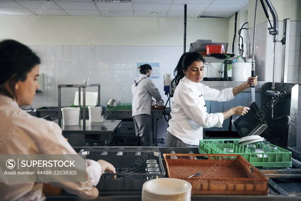 Female chef washing dishes in commercial kitchen