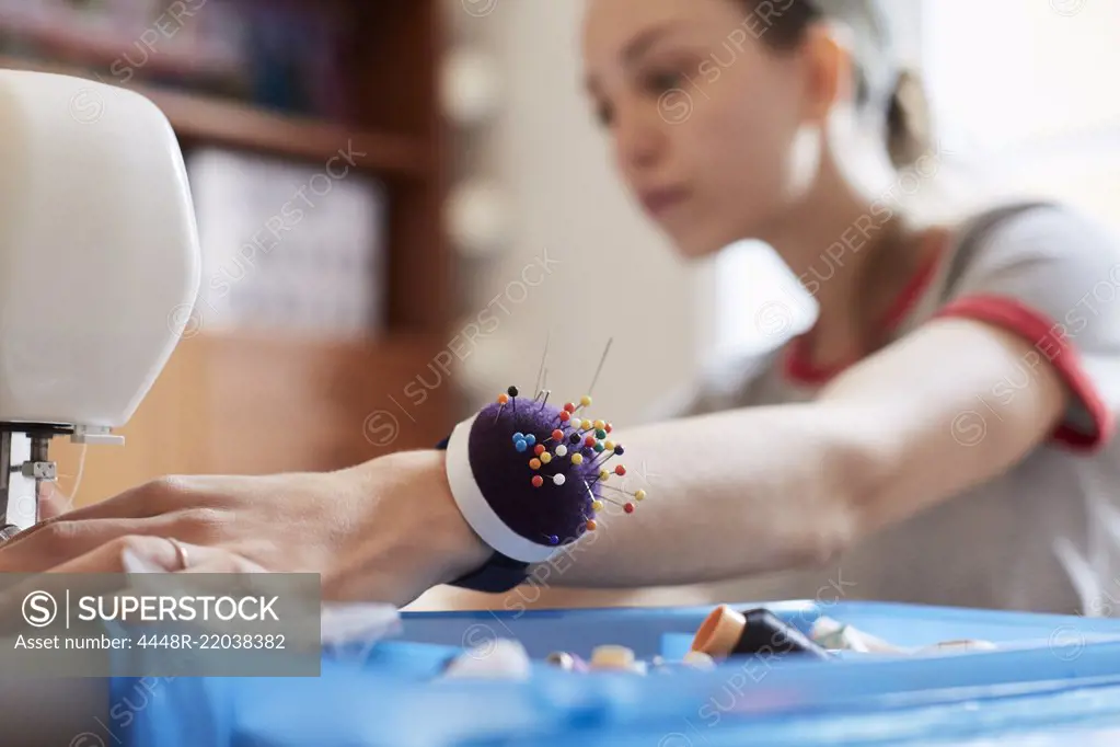 Close up of female tailor wearing pin cushion on wrist while using sewing machine at table