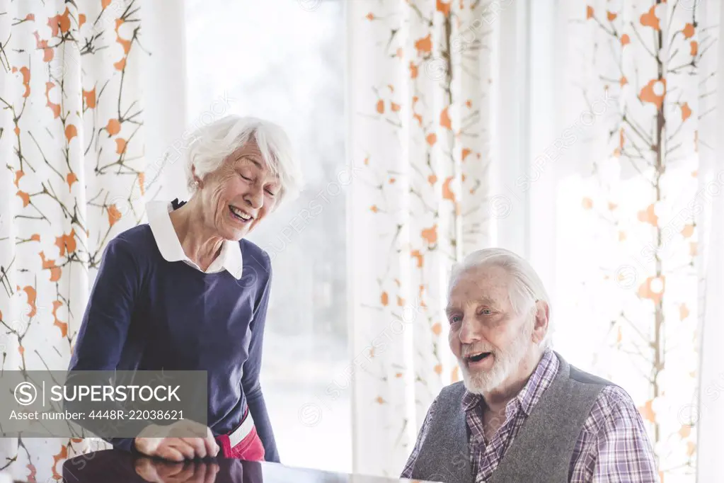 Senior man playing piano while woman singing in nursing home