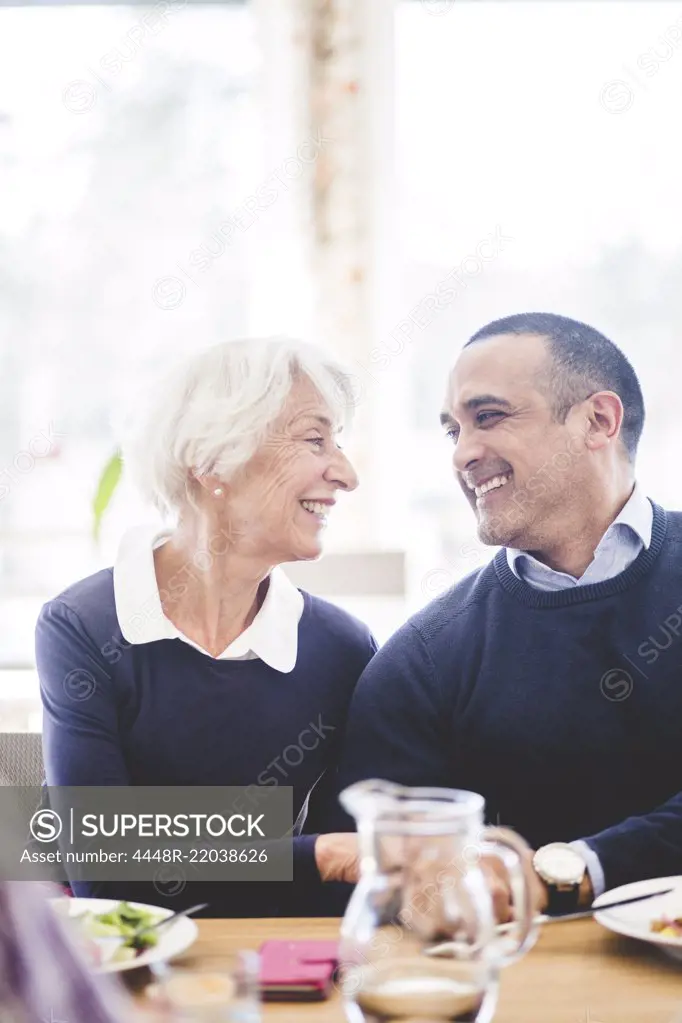 Cheerful senior man sitting face to face with son while having lunch at table in nursing home