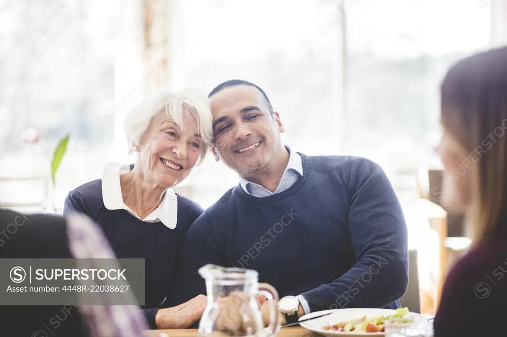 Smiling senior woman sitting with son while having lunch at table in nursing home