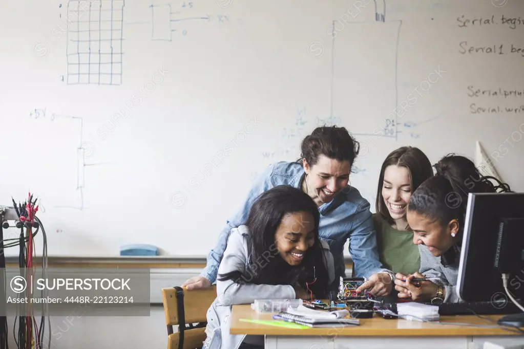 Smiling female teacher and high school teenage students preparing robot on desk in classroom