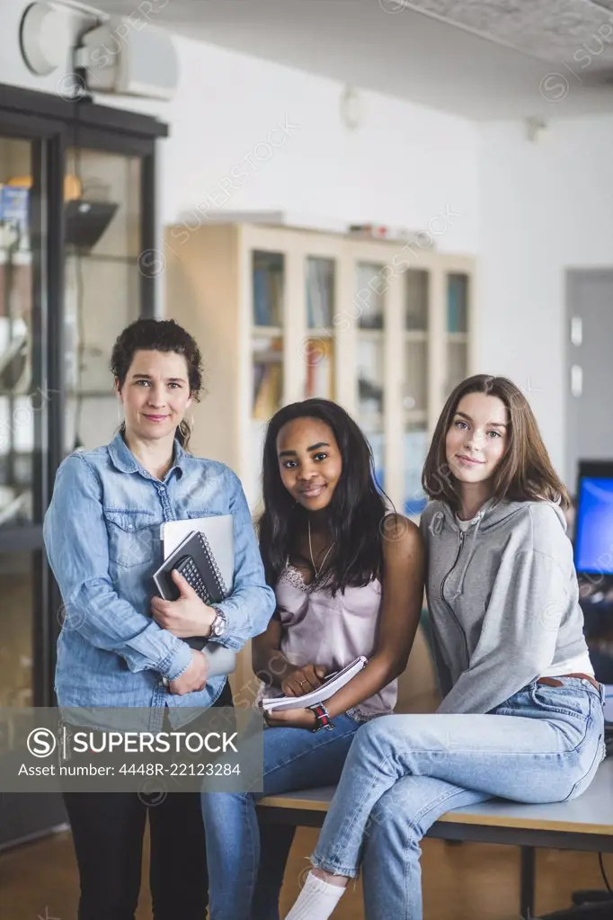 Portrait of confident female teacher standing by high school students in computer lab