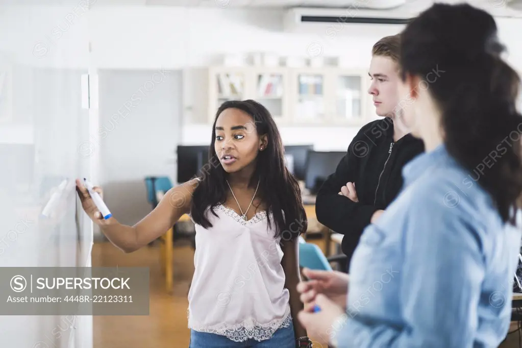 Confident girl explaining from whiteboard to teacher and friend in classroom