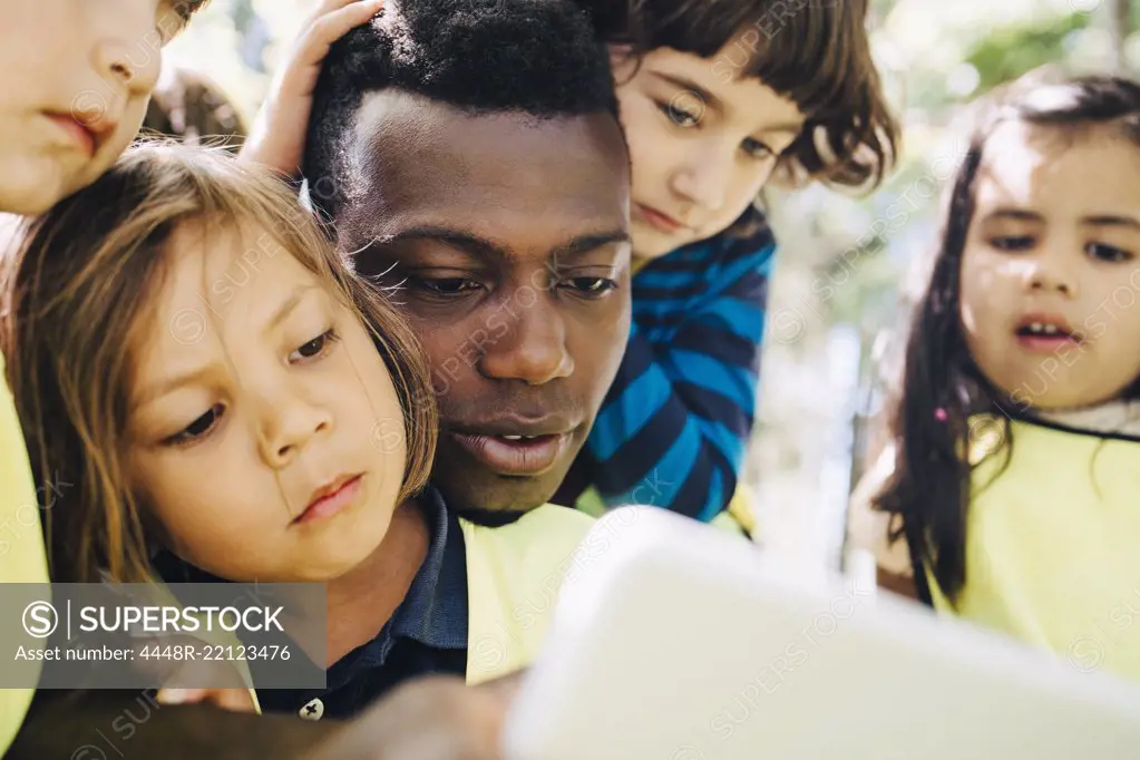 Male teacher sharing digital tablet with students in playground