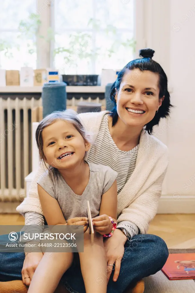 Portrait of smiling girl sitting on teacher's lap in kindergarten classroom