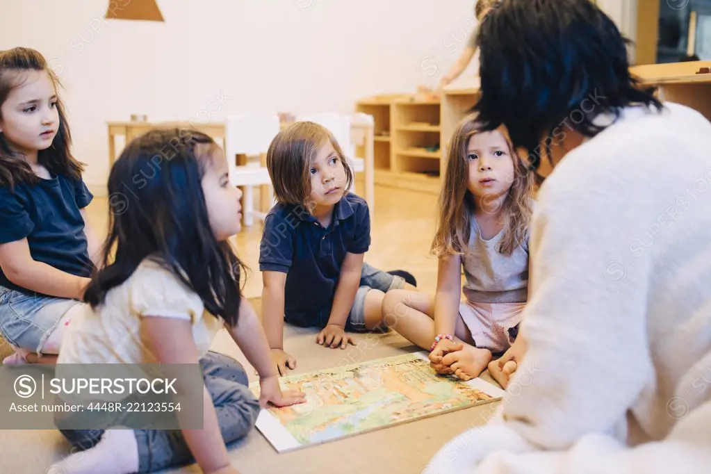 Female teacher telling story to students sitting in classroom at child care