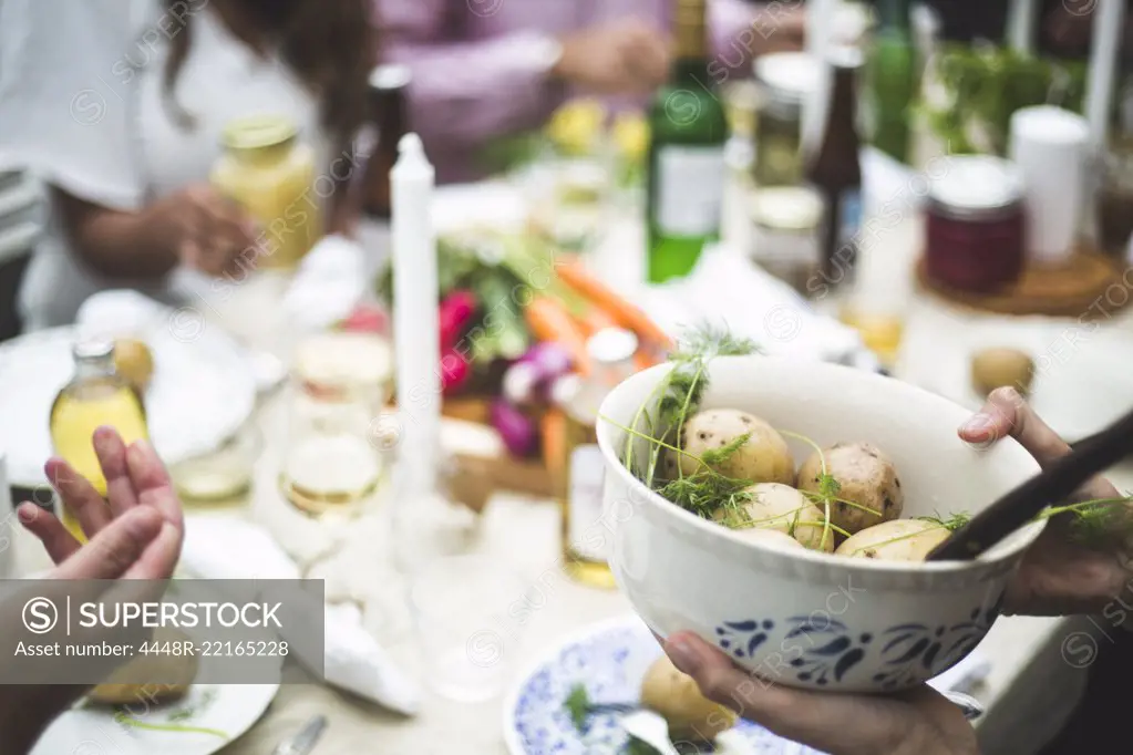 Cropped image of woman holding boiled potatoes bowl at dining table during dinner party