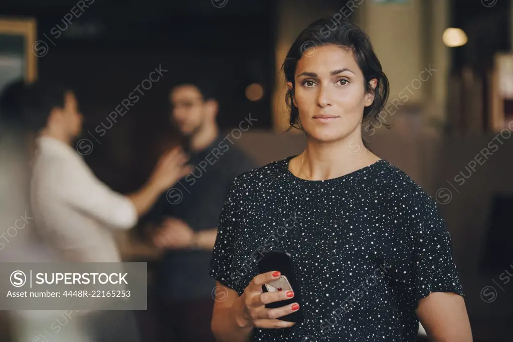 Portrait of confident businesswoman holding mobile phone in creative office