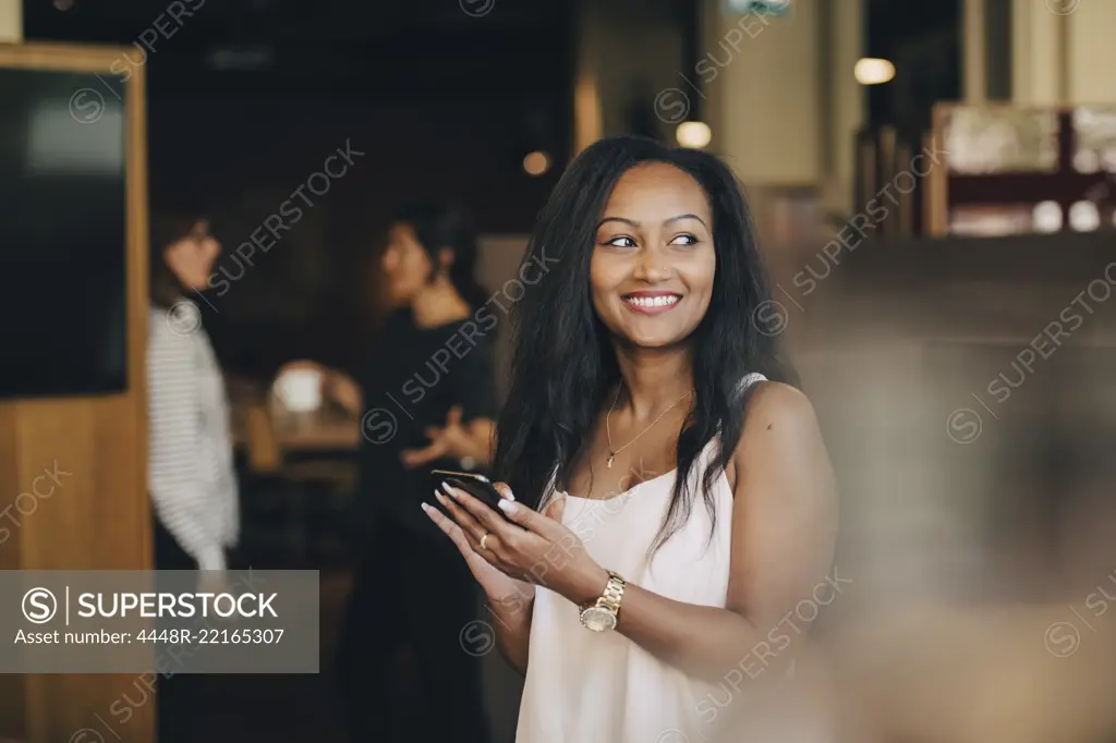 Smiling young businesswoman using smart phone in office