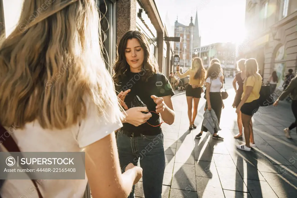 Women looking at camera while friends standing in background during sunny day