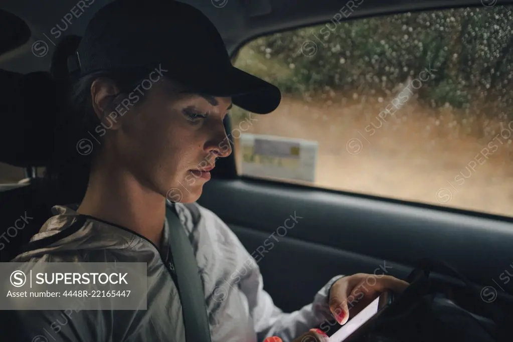 Female athlete using mobile phone while traveling in car during rainy season