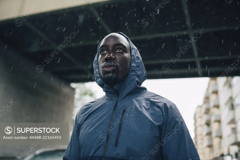 Low angle view of sportsman looking away while standing against bridge during rainy season