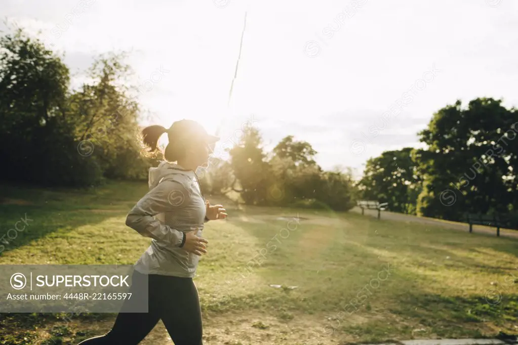 Side view of female athlete jogging at park during sunny day