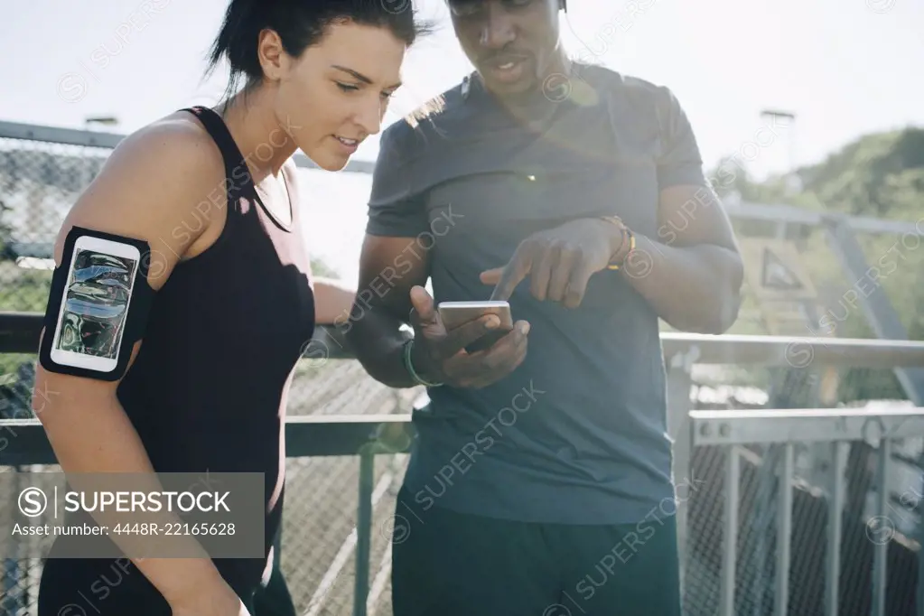 Sportsman showing mobile phone to female athlete while standing by railing on bridge