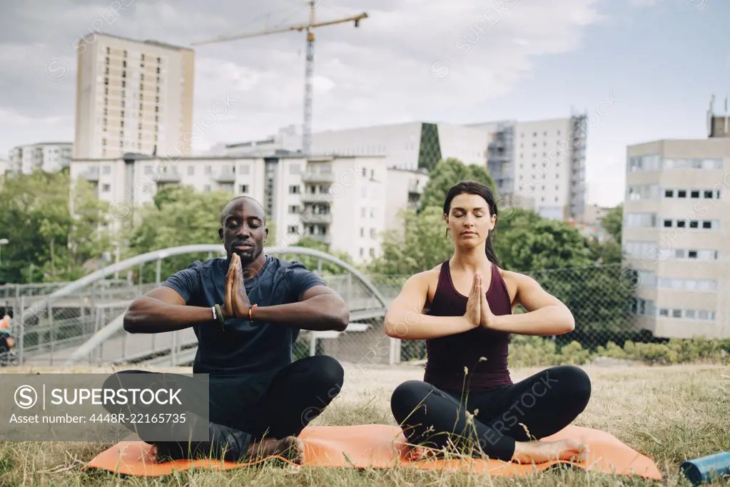 Multi-ethnic friends practicing yoga on field against buildings in city