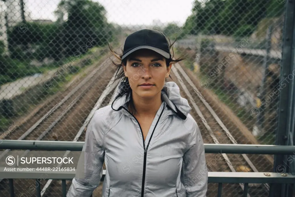 Portrait of confident female athlete standing against railing on bridge