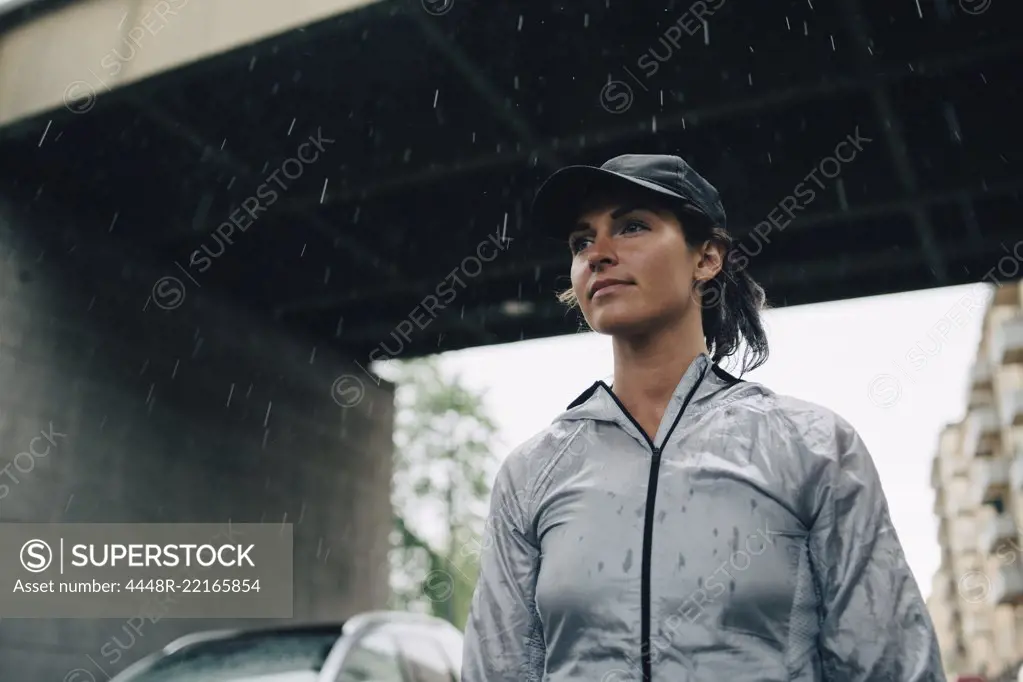 Low angle view of female athlete looking away while standing against bridge during rainy season