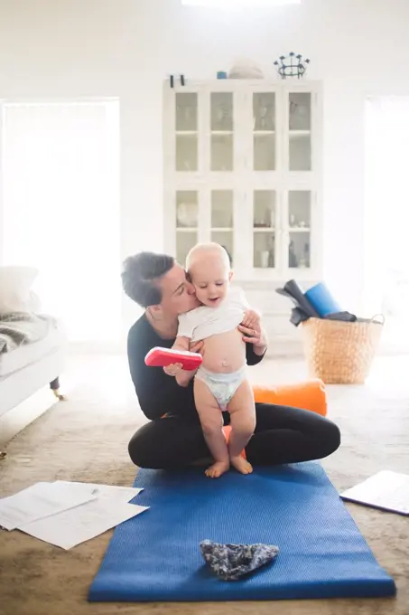 Female entrepreneur kissing daughter while practicing yoga in living room at home