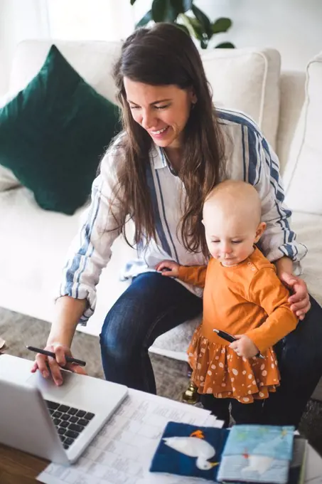 High angle view of smiling businesswoman telecommuting while sitting by daughter on sofa in living room