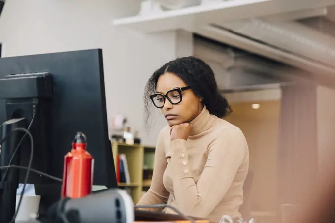 Focused female computer programmer working on laptop at desk in office