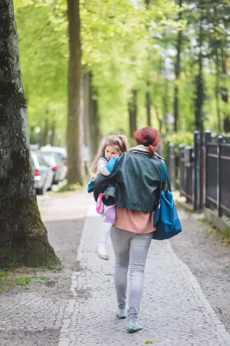 Rear view of mother carrying daughter while walking on footpath